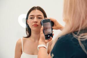 Using smartphone. Getting photo rejuvenation procedure at cosmetology clinic. Women in beauty salon
