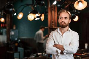 Standing with arms crossed.. Handsome barber is in the salon photo