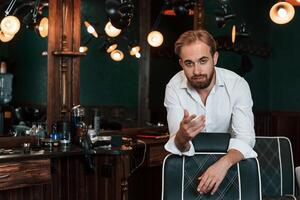 Leaning on the chair. .Handsome barber is in the salon photo