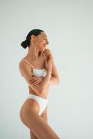 Relaxed,, standing, against white background. Young woman with slim body type is in fitness clothes in the studio photo