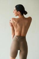 Back view, showing the spine, without bra. Young woman with slim body type is in fitness clothes in the studio photo