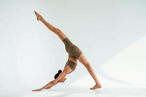 Working on the ,stretching of legs. Young woman with slim body type is in fitness clothes in the studio photo