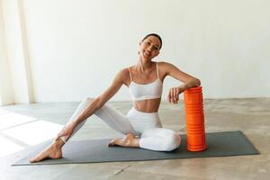 With orange colored foam roller., Young woman with slim body type is in fitness clothes in the studio photo