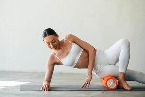 Using foam roller for exercises. Young ,,woman with slim body type is in fitness clothes in the studio photo