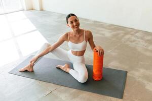 With, orange, colored foam roller. Young woman with slim body type is in fitness clothes in the studio photo