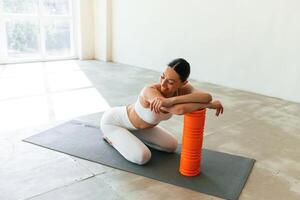 Sitting with foam roller.. Young, woman with slim body type is in fitness clothes in the studio photo