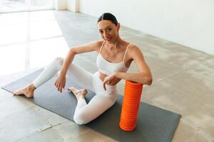 Sitting ,with foam roller. Young woman with slim body type is in fitness clothes in the studio photo