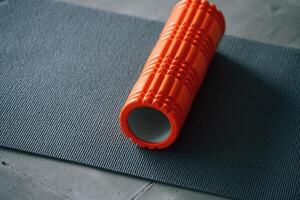 Close, up view of yoga mat and orange colored foam roller for spine exercises photo