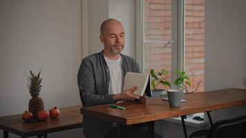A middle-aged man in a home setting, sitting at a table. He is in a good mood and feeling inspired as he writes down ideas for a story in a notebook. The scene reflects a creative atmosphere. video