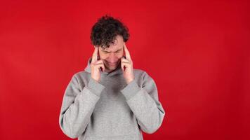 agonized curly man in gray hoodie massaging temples and bridge of nose, suffering from burnout work. Isolated on red background of studio shot. concept - mental health, fatigue, headaches video
