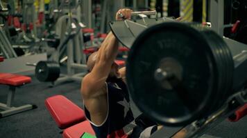 bald athletic man beard performs leg exercises using machine in gym. He is concentrated on his workout while surrounded equipment and weights during daytime video