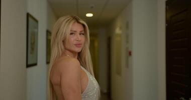 striking blonde woman walks gracefully down a well lit corridor. As she reaches the end she turns and faces the camera with a charming smile and an air of confidence video