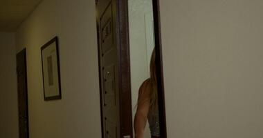 beautiful blonde woman opens a front door and steps outside into a well lit hallway. The setting features clean lines and minimal decor enhancing the modern look video