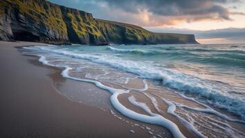 Ocean Waves Lapping on Sandy Beach with Grassy Cliff Backdrop photo