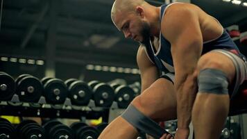 In well equipped gym bald athletic man beard engages in leg exercises. He adjusts his wraps while seated displaying determination and strength video