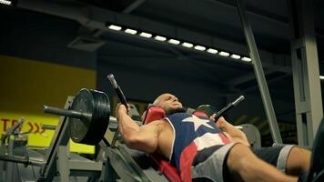 bald athletic man beard is focused on leg workouts in spacious gym. He is using leg press machine and demonstrating impressive effort video