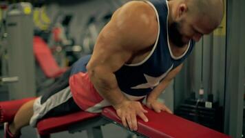 Bald athletic man beard engages in leg exercises using gym equipment. He focuses intently on his workout in modern fitness center during evening hours, does leg curls video