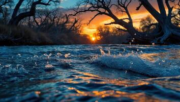 River Flowing at Sunset with Bare Trees and Vibrant Sky photo