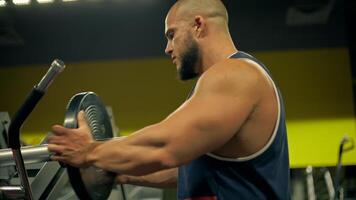 athletic bald man beard is engaged in leg exercises gym. It is evening as he works out intensely focusing on puts weight on the machine video