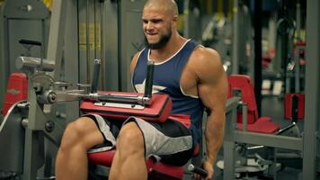 bald athletic man beard engages in leg exercises gym. He focuses on does leg extensions video