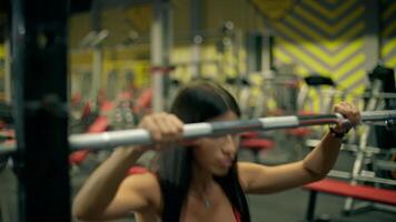 beautiful athletic woman is engaged in a strength training session at the gym squatting on a smith machine while wearing a red top and leggings. She focuses on maintaining proper form video
