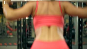 Athletic woman squats on a smith machine at gym dressed in a form fitting red top and leggings. Her focus is on maintaining proper form while building strength video
