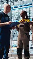 Vertical Smart factory engineering team coworkers oversee operation of robotic arms on facility floor. Industry 4.0 plant teamworking colleagues monitor system performance and troubleshoot issues, camera A video