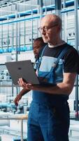 Vertical Industry 4.0 industrial plant senior engineer automating robotic machines using laptop software. Experienced technician implementing AI features in smart factory using notebook, camera A video