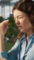 Vertical Woman suffering from migraine at work, reading medication prescription. Employee experiencing headache while reviewing financial charts on computer monitor at office desk, camera A video