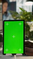Vertical Close up of green screen tablet in front of employee checking progress done on project. Chroma key device next to office clerks reading data statistics on PC screen, camera A video
