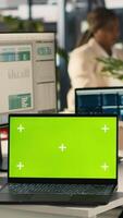 Vertical Green screen mockup laptop next to accountant inputting financial figures on PC after checking reports. Chroma key notebook next to businesswoman working in office, crosschecking data, camera A video