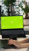 Vertical Office clerk uses chroma key devices to read data statistics on display after audit. Employee at work using green screen laptop and tablet to check progress done on commissioned project, camera A video