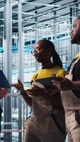 Vertical Industry 4.0 photovoltaics plant senior engineer reading paperwork talks with workers to maximize power generation. Solar panels smart factory experienced leader giving tasks to technicians, camera A video