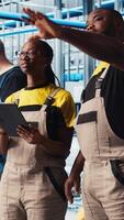 Vertical Smart factory coworkers talking, working together to test automated systems. Industry 4.0 industrial plant teamworking colleagues identify bottlenecks and optimize gear based on data, camera A video