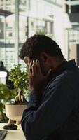 Vertical Worker feeling painful headache while working, suffering burnout while rushing to finish tasks before deadline. African american man in office having migraine after working overtime, camera B video