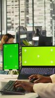 Vertical Isolated screen laptop and tablet on office desk next to employee editing documents on computer. Chroma key devices next to worker analyzing data charts, interpreting statistical information, camera B video