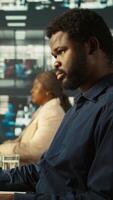 Vertical Close up of worker in office using landline phone to talk with customer. African american employee at work discussing with business partner during call, analyzing performance metrics, camera B video