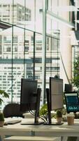 Vertical Modern office workspace desk with computer monitors displaying graphs, charts and data analytics, surrounded by plants and paperwork with city environment background, panning shot video
