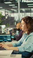 Vertical Woman suffering from migraine at work, reading medication prescription. Employee experiencing headache while reviewing financial charts on computer monitor at office desk, camera B video