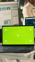 Vertical Green screen laptop on office desk next to employee editing documents on computer. Mockup notebook next to worker analyzing data charts, interpreting statistical information, camera A video
