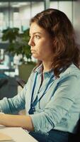 Vertical Close up of woman sitting at office desk, solving tasks during job shift. Office clerk doing email communication in workplace, researching data for company project, camera B video
