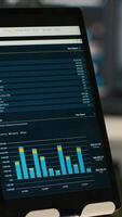Vertical Close up of tablet screen on desk displaying financial graphs of company profits performance metrics. Data analytics on device display showing corporate business earnings KPIs video
