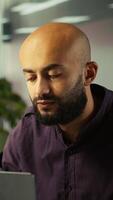 Vertical Smiling employee in warm office working on company project, multitasking. Cheerful freelancer answering emails, typing on keyboard, working in modern workplace, camera B close up video