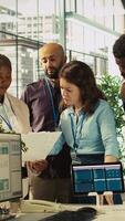 Vertical Portrait of smiling coworkers looking over revenue figures on paperwork in office. Happy team of accountants focused on comparing company statistical numbers to finish job before deadline, camera B video