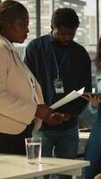 Vertical Employee with paraplegia and colleagues in inclusive office brainstorming, reviewing financial charts, analyzing KPIs. Person with paraplegia and team coworkers colleagues comparing data, camera B video