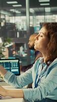 Vertical Worker in office using landline phone to talk with client while reviewing charts. Employee at work discussing with business partner during call, analyzing business performance metrics, camera B video