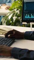 Vertical Close up of worker in office using landline phone to talk with customer. African american employee at work discussing with business partner during call, analyzing performance metrics, camera A video