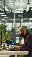 Vertical Arab man in office reviewing financial graphs, analyzing key performance indicators. Middle Eastern employee in workspace looking over data trends and strategic insights, camera B video