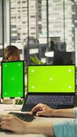 Vertical Office clerk uses chroma key devices to read data statistics on display after audit. Employee at work using green screen laptop and tablet to check progress done on commissioned project, camera B video