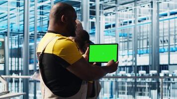 Smart factory engineer oversees operation of robotic arms and conveyor belts using green screen tablet. Industry 4.0 plant technician monitors system performance using chroma key device, camera A video